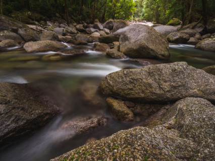 Long exposure of water flowing around rocks in fast moving river. Mossman, Queensland, Australia