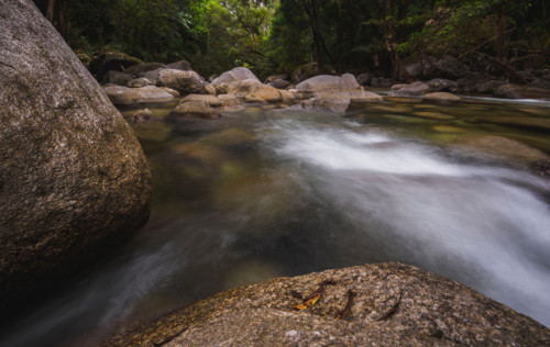 Long exposure of water flowing around rocks in fast moving river. Mossman, Queensland, Australia