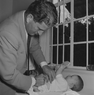 Changing Tubby Block's baby. Tubby Block's baby plays with a hairbrush whilst a man in a jacket and