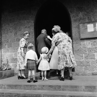 Ushered in. Two smartly dressed women usher a young boy and girl into a church on the occasion of