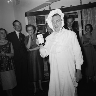 Baby costume. A man wears a fancy dress baby costume at the Archer's New Year party. He holds a