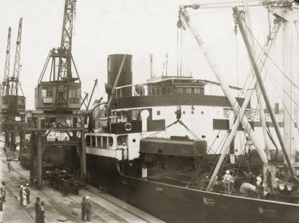 Unloading a locomotive tender from SS Harmonides. Cranes onboard the SS Harmonides hoist a