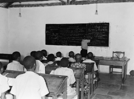 Kenyan school room. A classroom of children sit in rows behind desks listening to a teacher who is