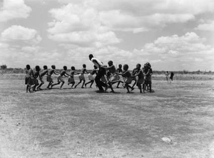 A train of children. A train of children wearing shorts hold onto one another as they run around in