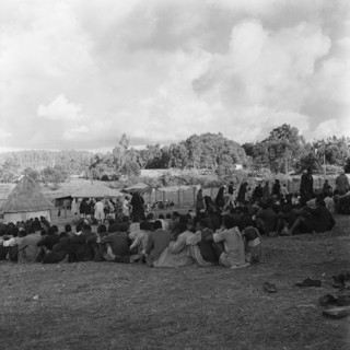 Prisoners in camp. Prisoners sit together in tightly packed lines in a fenced camp watched over by