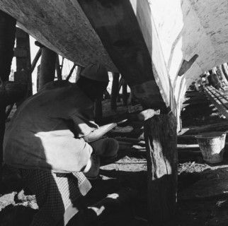 Dhow under repair. A workman hammers the underside of a dry-docked dhow. Zanzibar (Tanzania), 3-12