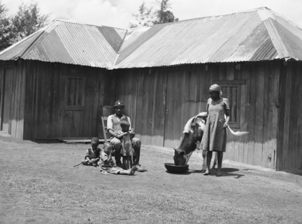 Headman Samuel and family. Headman Samuel sits surrounded by three young children outside a small