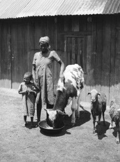 Headman Samuel's wife. Headman Samuel's wife stands next to a young boy wearing a plain dress and