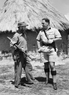 Davo' Davidson with police chief. Davo' Davidson stands outside a mud hut with a uniformed police