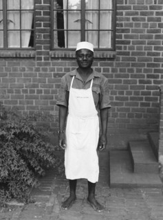 Price's room boy. The Price family's room boy pictured barefoot outside a brick building. He wears