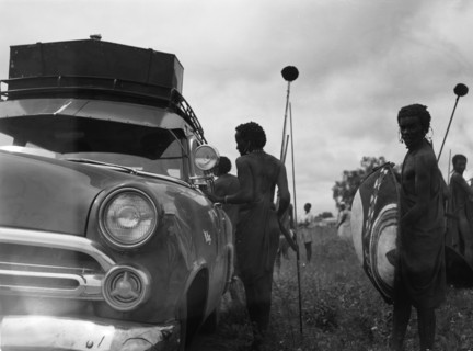 Maasai and Ford. Maasai warriors holding spears and shields congregate on the roadside near a Ford