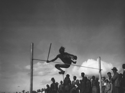 High jump. A man holding a baton attempts the high jump at a 'ngoma', a word meaning drum that is