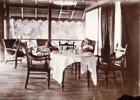 Colonial veranda. A European man smokes a cigar as he reclines in a chair on a colonial veranda.