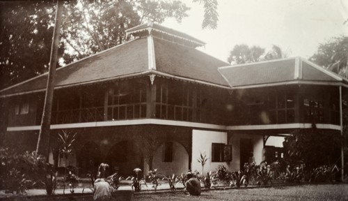 Colonial bungalow, Burma (Myanmar). Servants at work tending flowerbeds beside the driveway of a