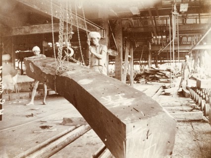 Manoevering teak logs at a timber yard. Two labourers manoeuvre a processed timber beam using a