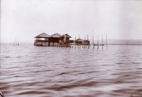 Lake dwellings in Burma (Myanmar). Two wooden dwellings on stilts project from the calm waters of a