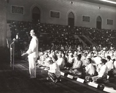 Addressing the sixth Buddhist Synod. A European man stands before a microphone, addressing a