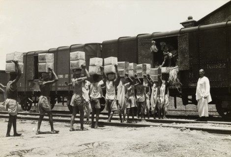 Queuing up to load a freight train. A team of workers carry boxes on their heads and form a queue,