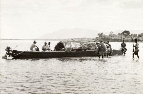 Boarding the District Commissioner's River boat. A European man is carried through shallow water to