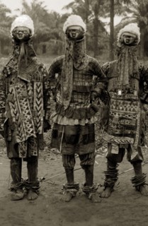 Juju practitioners. Three juju dancers in costume wear wooden masks on top of their heads, ornate