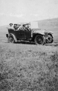 Car crosses the veldt. Five European men in an open-topped car drive along a rough track in