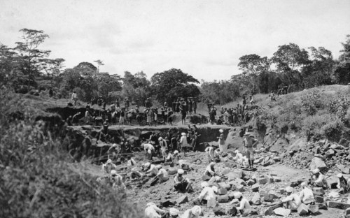 Stone quarry. A European man stands in the centre of a shallow quarry surrounded by African and