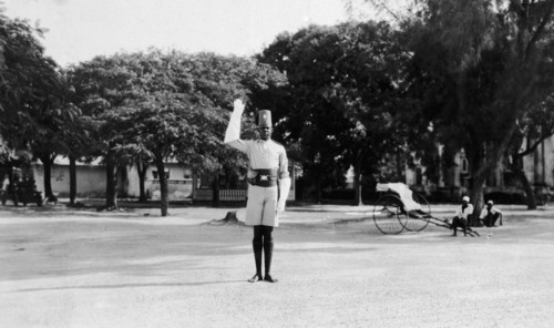 Kenyan traffic policeman. The policeman signals 'stop' with his white glove. Behind him two