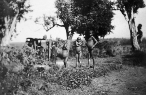Nandi children. Several young, naked Nandi children stand in front of a small maize mill operated