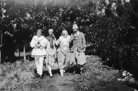 Christmas fancy dress. Four Europeans stroll arm-in-arm down a garden path wearing fancy dress.