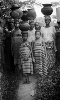 Carrying pots. Several Nigerian women and a young girl wear wraparound blankets and balance large