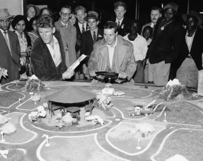 Driving game. A mixed race crowd gathers around a detailed miniature road model at the Motor Sports