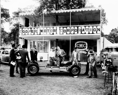 Cooper Motor Corporation. A group of European men chat beside the bare chassis of a car at the