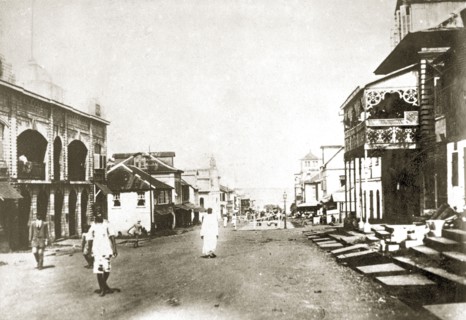 Sierra Leone street scene. A handful of people mill about on a wide road in the centre of a large
