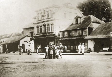 A main street in Sierra Leone. Africans and Europeans mill about on a wide main road in the centre