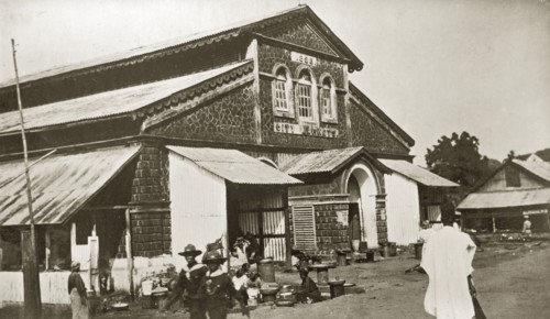 City market, Sierra Leone. A handful of people mill about outside a large stone market building in