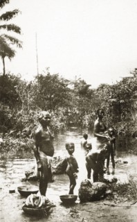 River laundry. A group of half-naked African women and children wash clothes in a shallow river