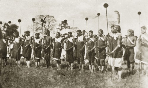 African dancers in costume. A group of African men dressed in ceremonial costume hold sticks as
