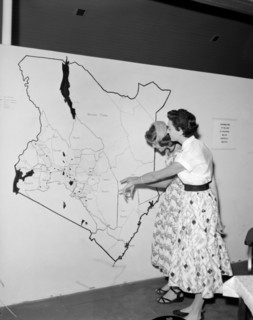 Map of Kenya at the KNFU stand. Two European women point at a large scale map of Kenya displayed at