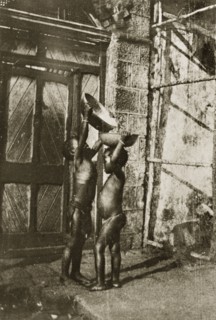 Young water carriers. A young child stretches up to pour water from one bowl into another balanced
