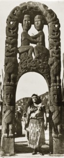 Beneath a Maori arch. A Maori woman in traditional dress stands beneath an ornate Maori arch that