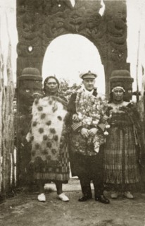 Rear Admiral Brand visits a Maori arch. Rear Admiral Sir Hubert Brand stands between two Maori