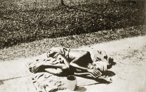 A India fakir in Ceylon. An Indian fakir lies hunched up with a begging bowl on a sack outside the