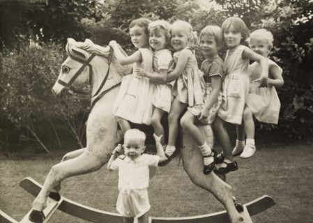 Alison's birthday party. Six smiling young girls sit astride a large rocking horse at 'Alison's