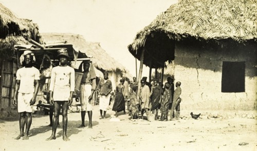 Gold Coast street scene. A group of men carry a sedan chair along a village street. Gold Coast