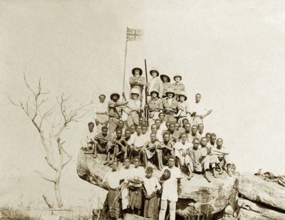 The flag on the rock. A union jack flag flies above a group of African and European Miller