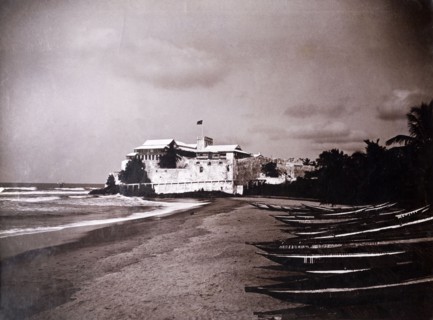 Christiansborg castle, Gold Coast. A line of canoes sit on a beach in front of Christiansborg