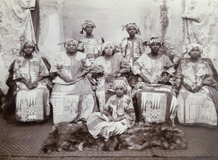 Eight women in indigo dresses. The women wear tailored gowns of dark cloth (probably indigo blue