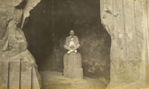 Inside the Elephanta Caves. A European man sits cross-legged, posing for the camera on a stone