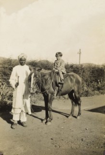 An Indian 'syce'. An Indian 'syce' (hostler) guides a pony ridden by a young British child along a