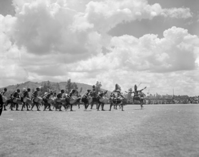 A line of Wakamba dancers. An audience watches as a long line of Wakamba men perform a dance with